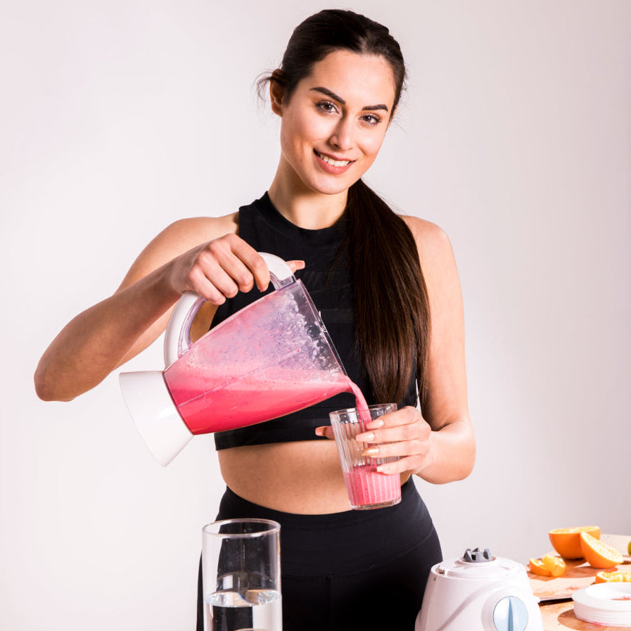 Woman pouring a pink smoothie into a glass against a white background